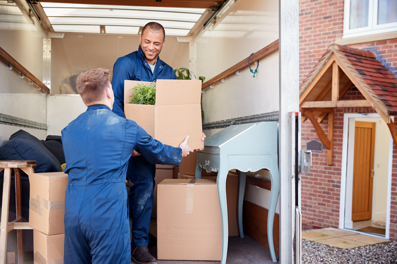 Office relocation team moving desks, chairs, computers, files, and packed equipment into a transport truck inside a modern corporate office building.