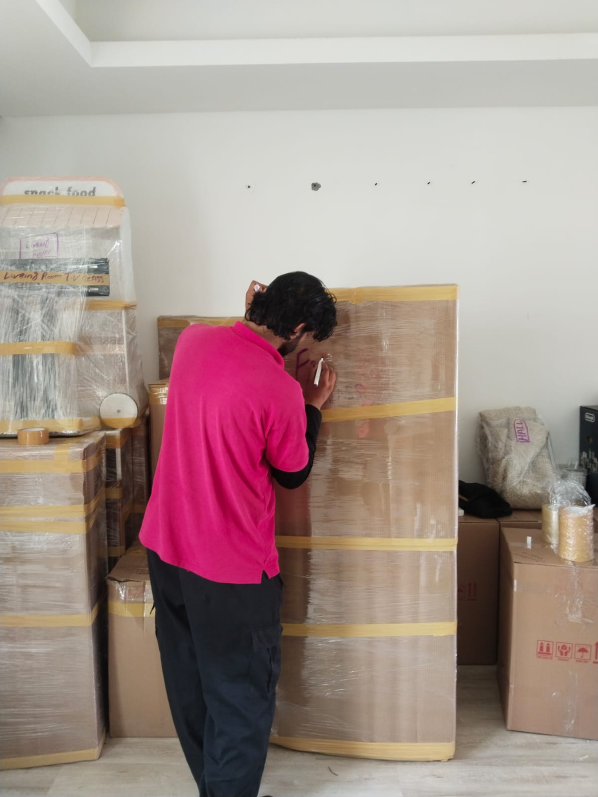 Packing and unpacking services in Dubai with a mover labeling a wrapped, taped box by room